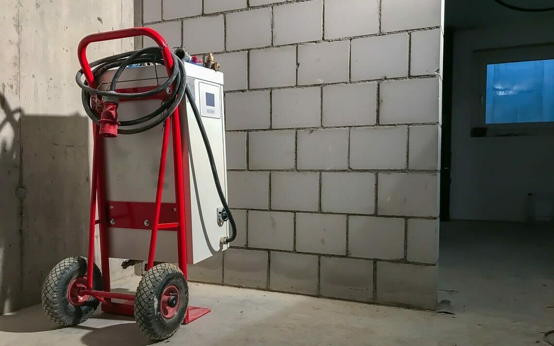 Mobile Elektroheizzentrale auf roter Sackkarre im Rohbau eines Hauses