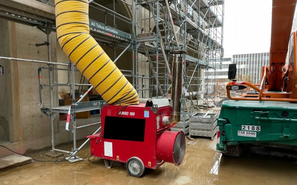 Mobile Bauheizung mit Abgasrohr und gelbem Lufttransportschlauch steht auf einer Baustelle