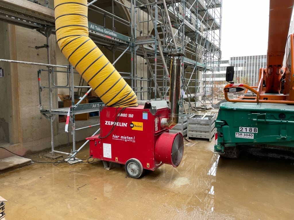 Rote mobile Bauheizung mit gelbem Lufttransportschlauch auf Baustelle