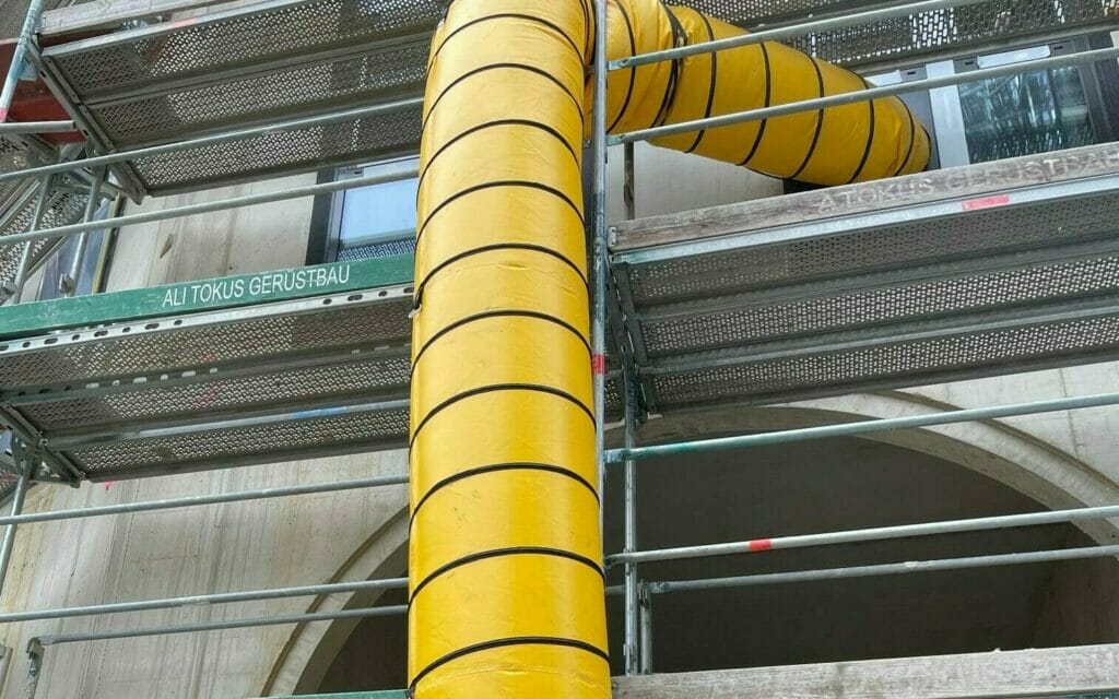 Gelber Warmlufttransportschlauch an Gerüst führt Wärme in die Baustelle