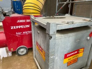 Mobiler Oeltank neben rotem Bauheizer auf Baustelle