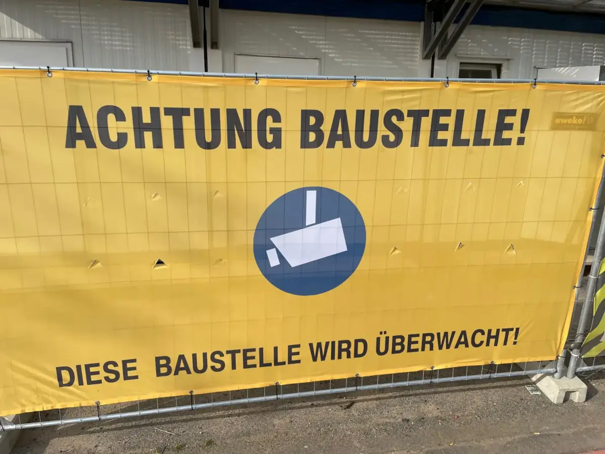Gelbes Baustellenueberwachung Warntransparent am Zaun einer Baustelle das vor Videoueberwachung warnt