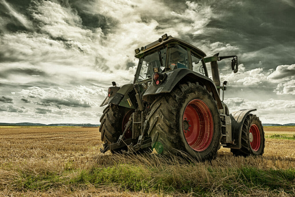 Grüner Traktor auf einem Feld mit sichtbarer Zapfwelle zum Anschluss eines Zapfwellengenerators