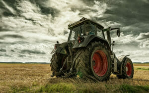 Grüner Traktor auf einem Feld mit sichtbarer Zapfwelle zum Anschluss eines Zapfwellengenerators