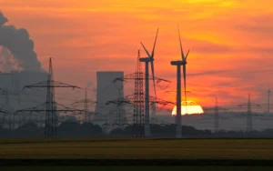 Windraeder stehen bei Sonnenuntergang vor Kohlekraftwerk und speisen Strom mit 50 Hz Netzfrequenz ins oeffentliche Stromnetz